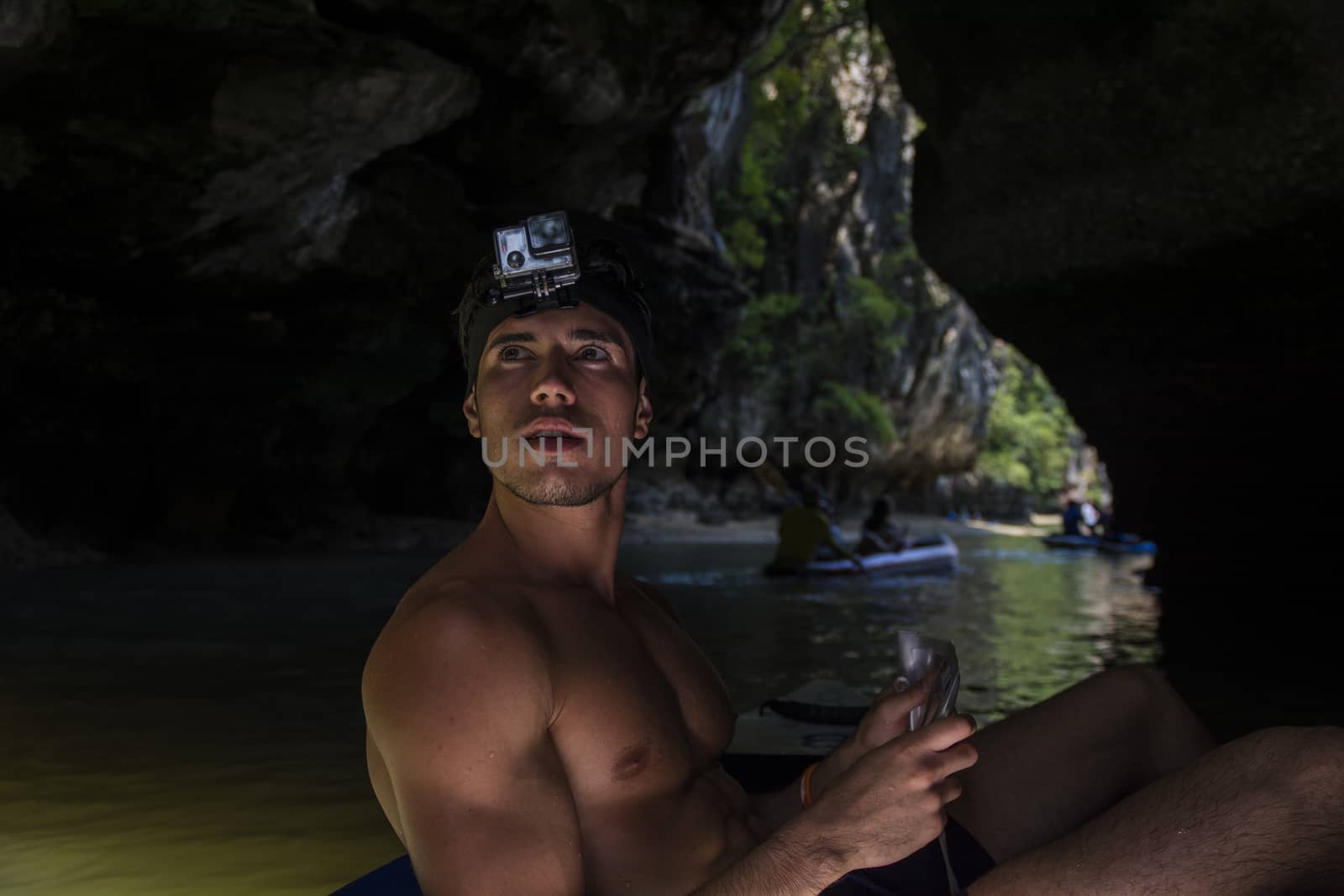 Rear view of a man on a raft relaxing drifting along the river in Phuket, Thailand, with action camera mounted on head, inside a cave on the water