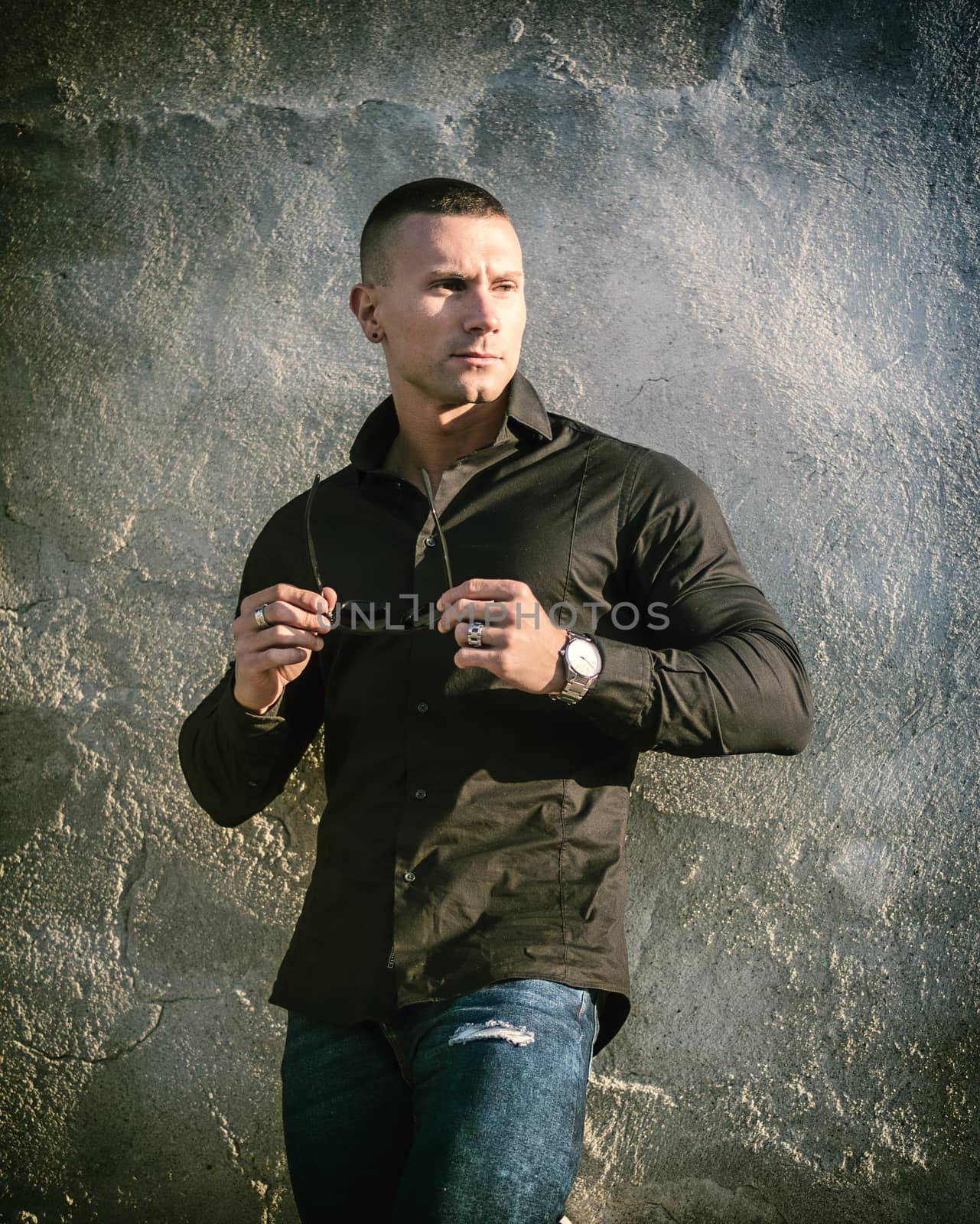 One handsome young man in urban setting in European city, standing, wearing black jacket and jeans