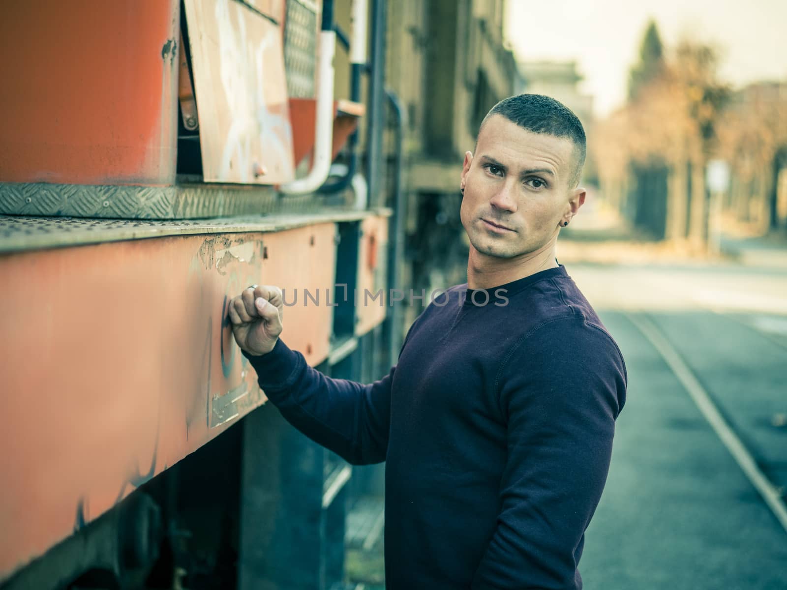 One handsome young man in urban setting in European city, standing, wearing black leather jacket and jeans