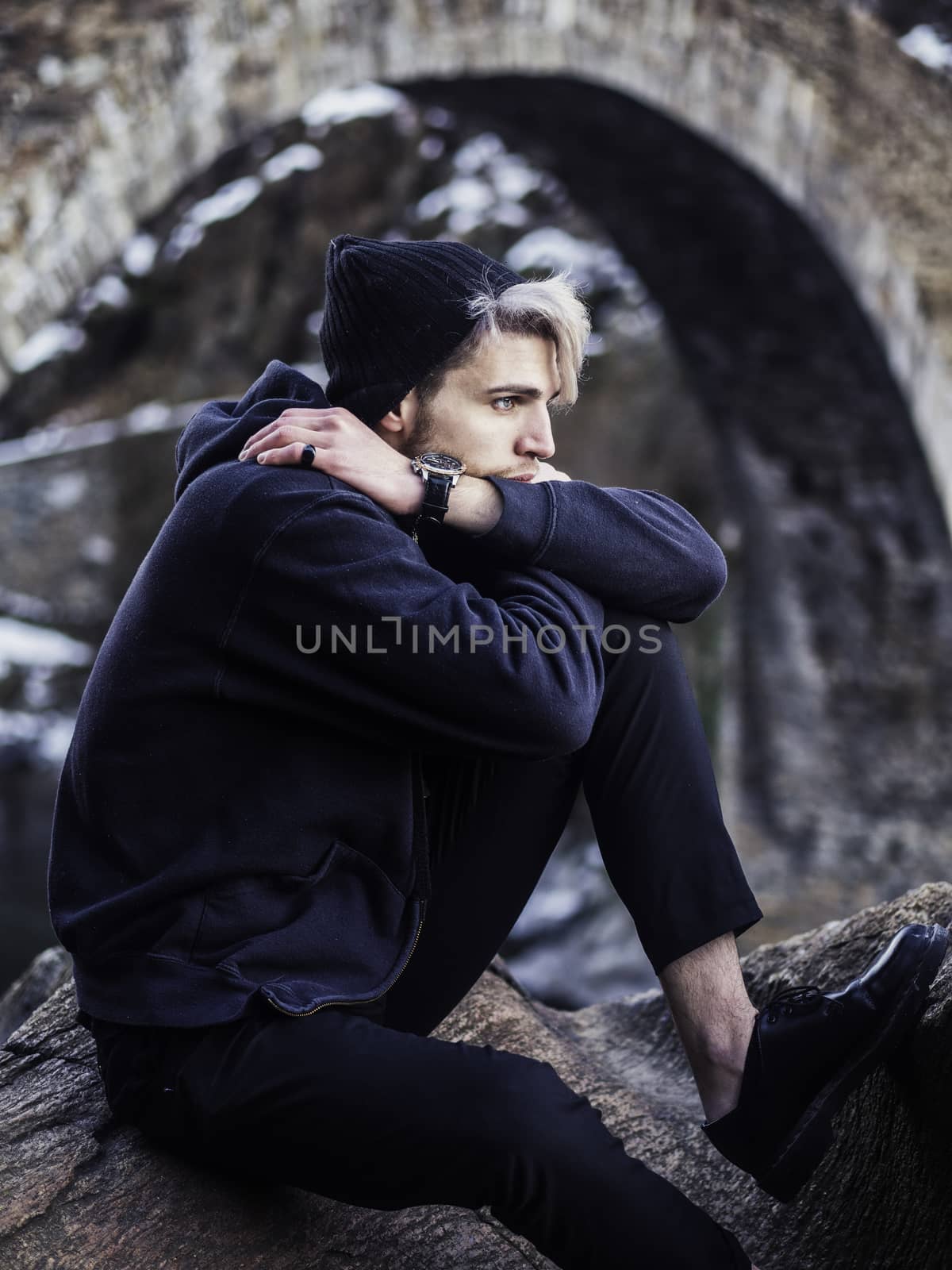 Portrait of young man in hoodie posing outdoor in winter setting with snow all around, looking away to a side.