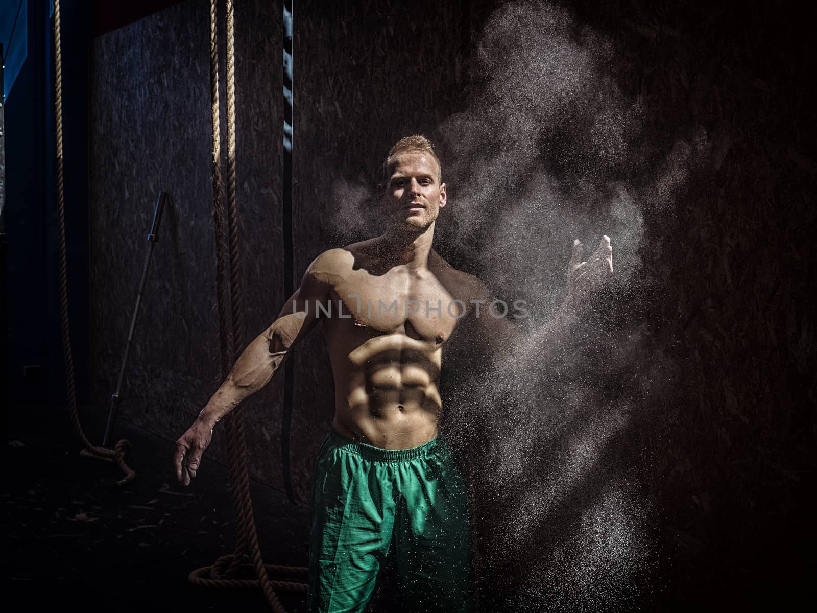 Shirtless man using chalk or magnesium powder in gym, clapping hands and creating cloud