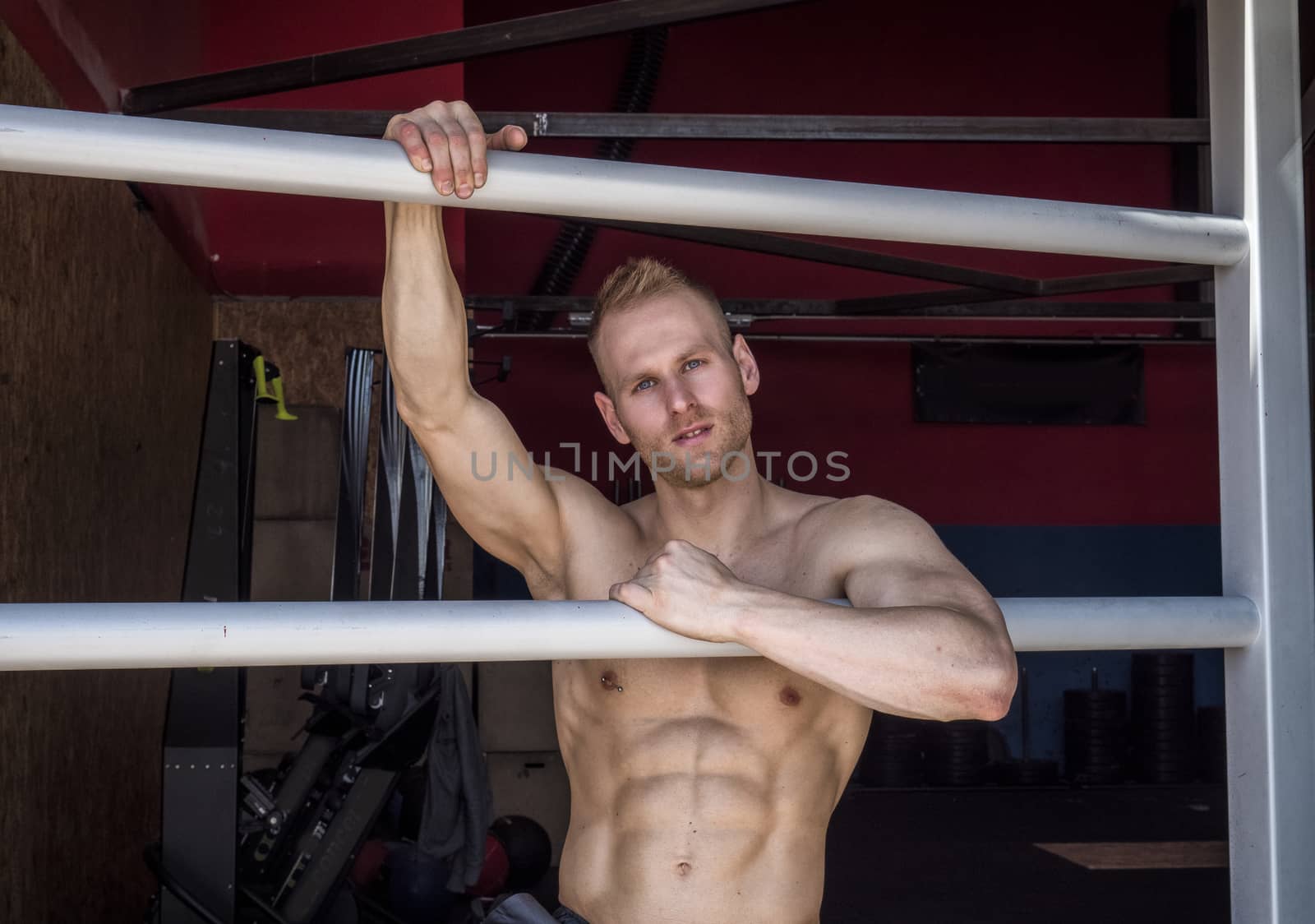 Handsome muscular young man standing against horizontal bars, looking at camera