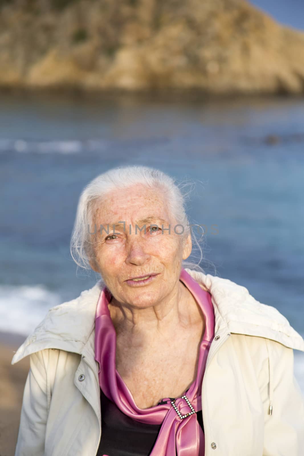 Portrait of the happy elderly woman against the sea in sunny spring day.