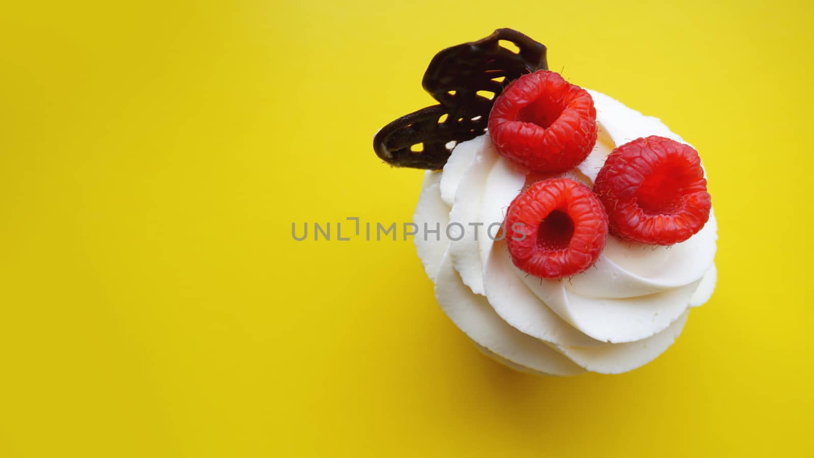 Homemade muffins with sweet cream and fresh red raspberries on a yellow background close up. Top view