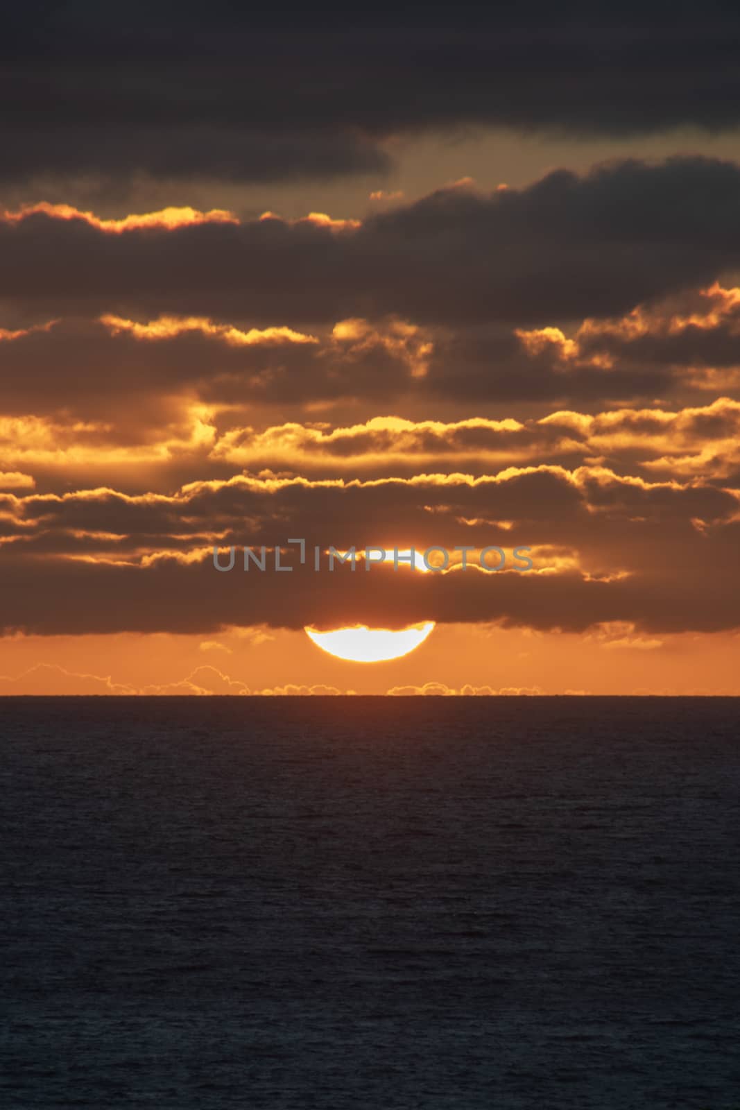 Sun nearly touching the horizon partly covered by red shining clouds by MXW_Stock