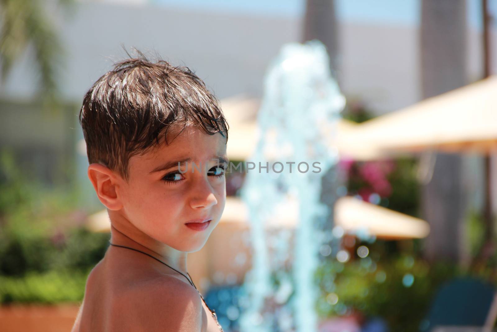 Little boy on the blurred background of a swimming pool with a fountain on holiday in a hotel on a sunny summer day.