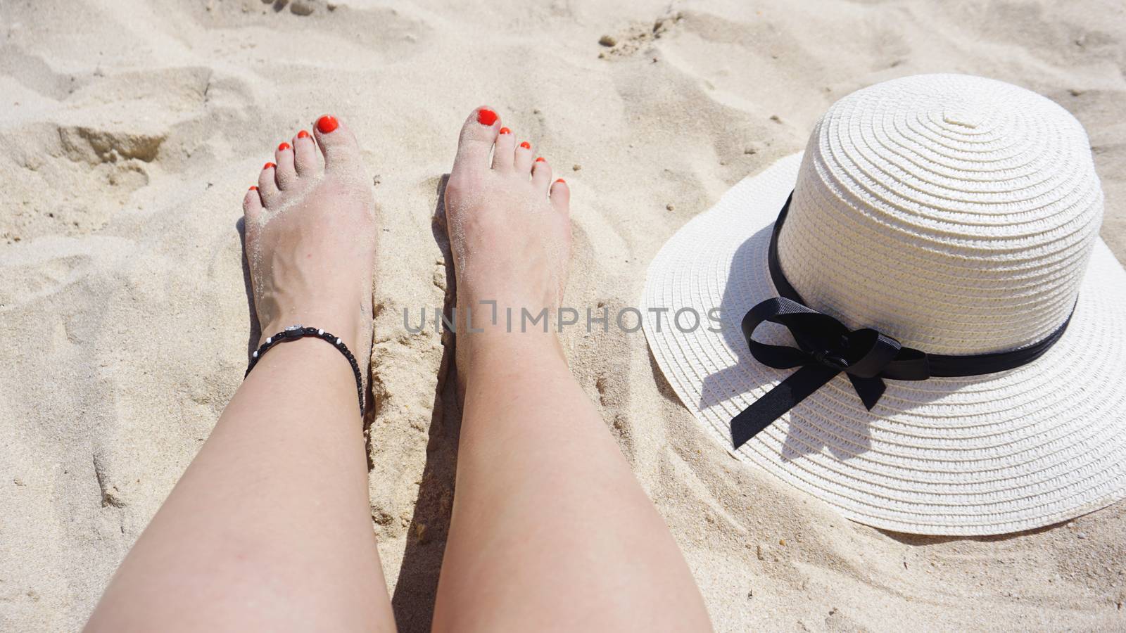 Summer holiday fashion concept - tanning woman legs and sun hat at the beach on a white sand