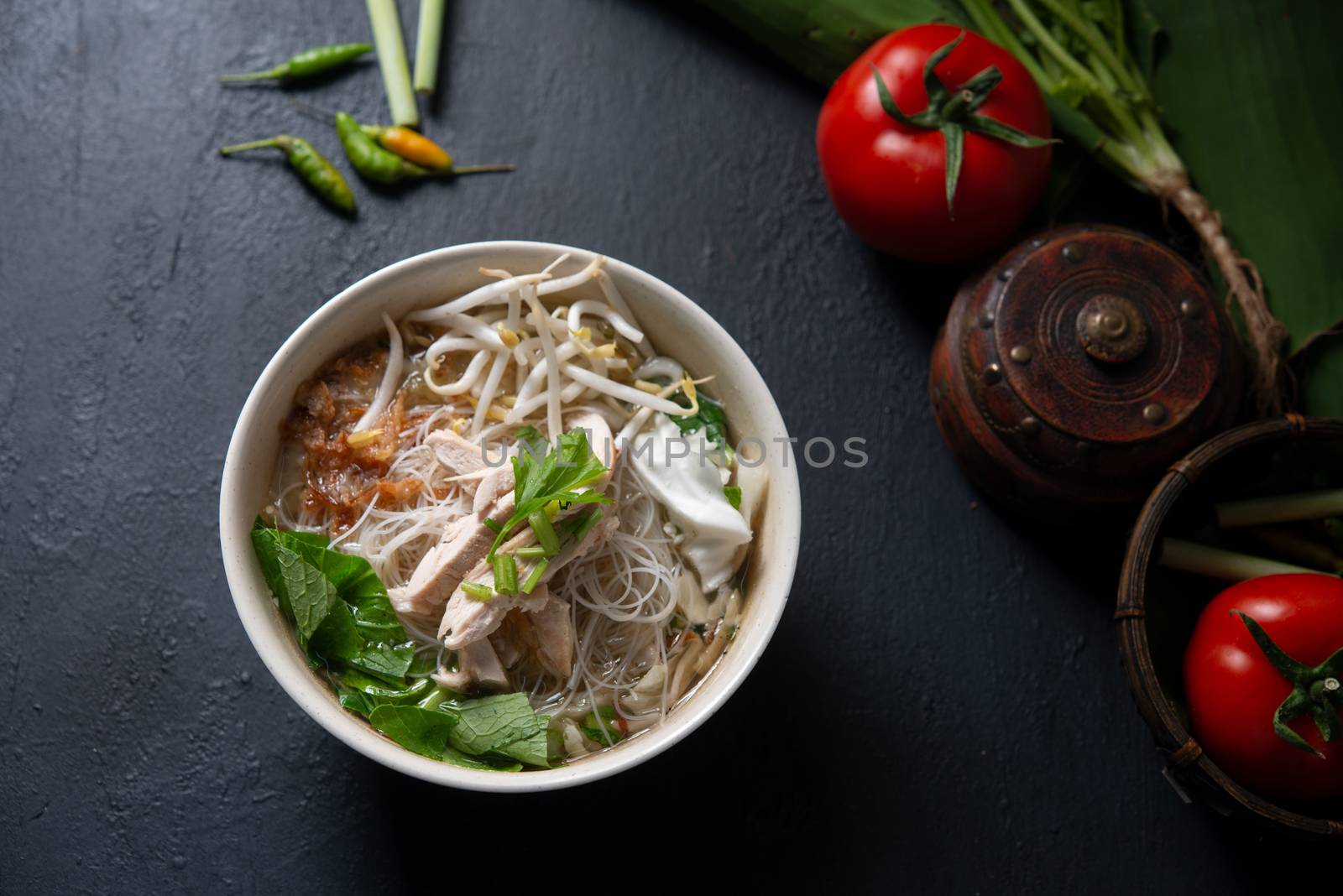 Asian rice noodles soup and chicken in bowl on dark background. Top view flat lay.