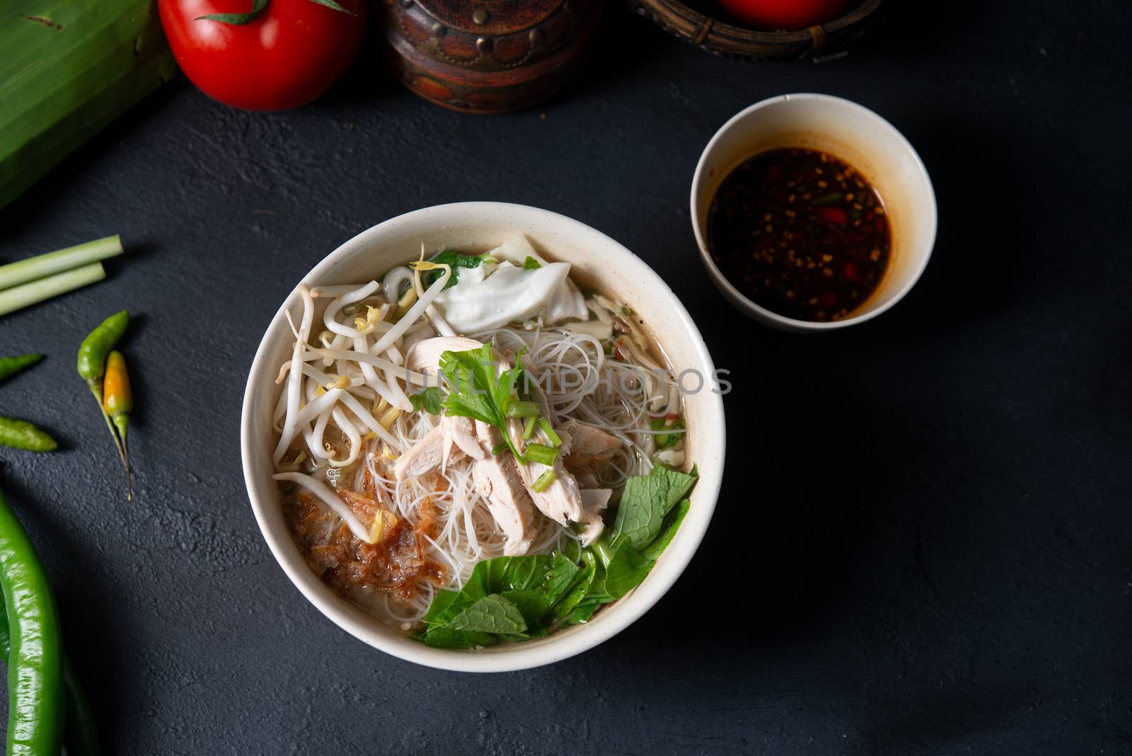 Asian rice noodles soup and chicken in bowl on dark background. Top view flat lay.