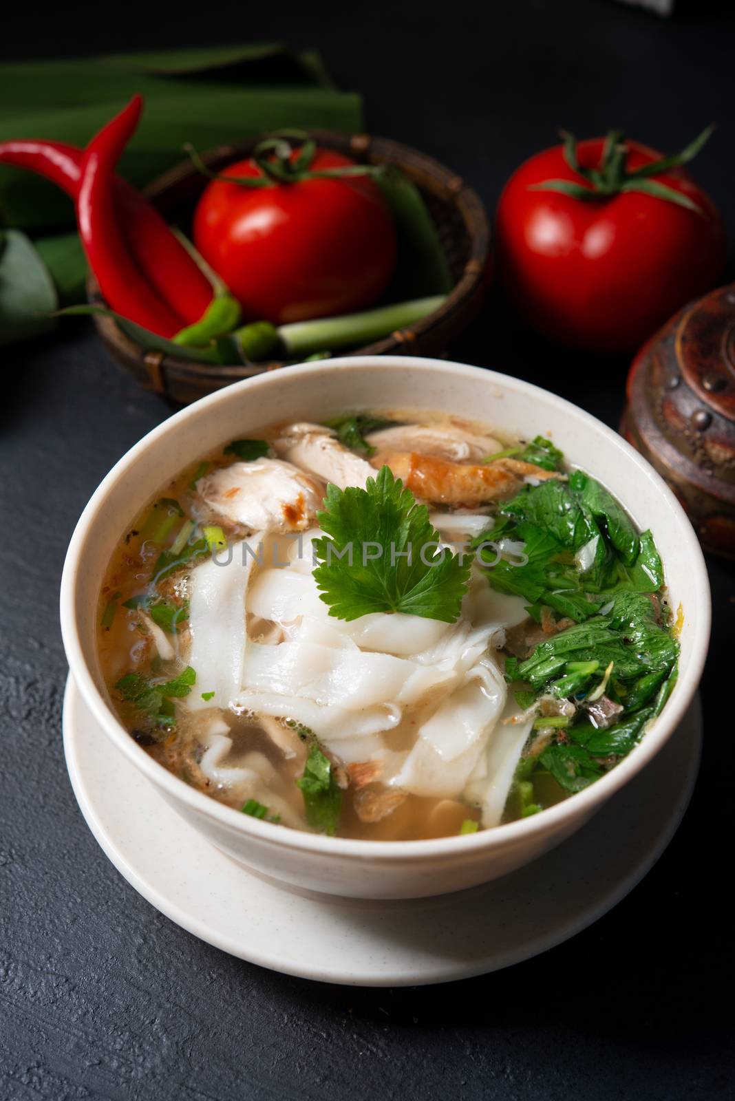 Asian kway teow soup noodle and chicken in bowl on dark background. 