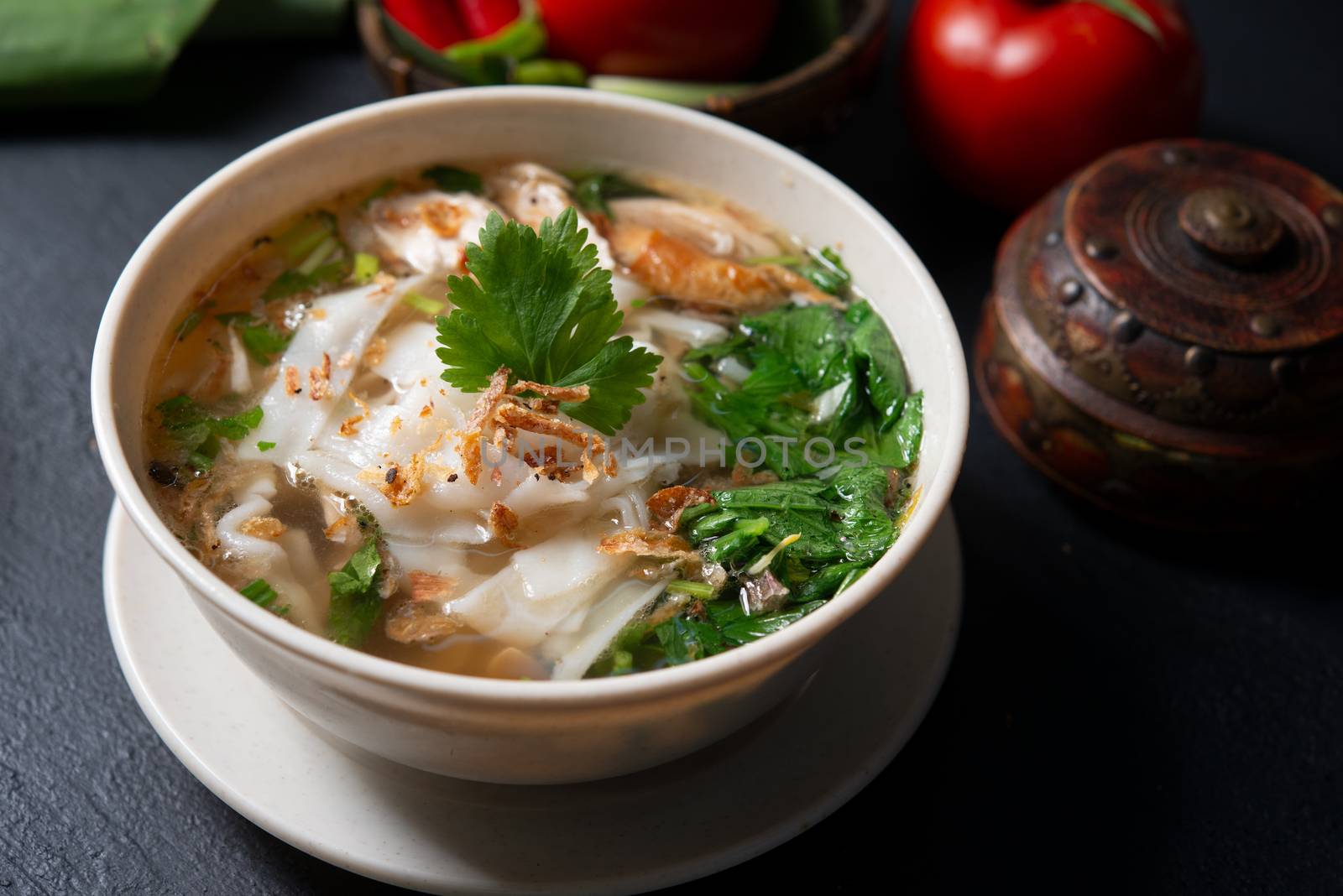 Asian kway teow soup noodle and chicken in bowl on dark background. 