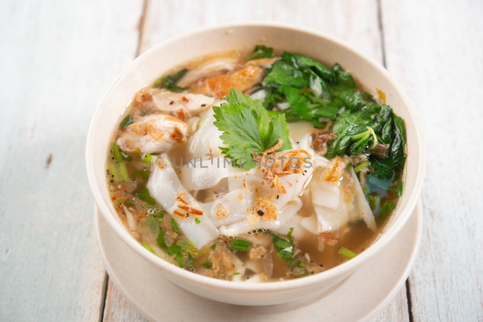 Asian kway teow soup noodle and chicken in bowl on wooden background. 
