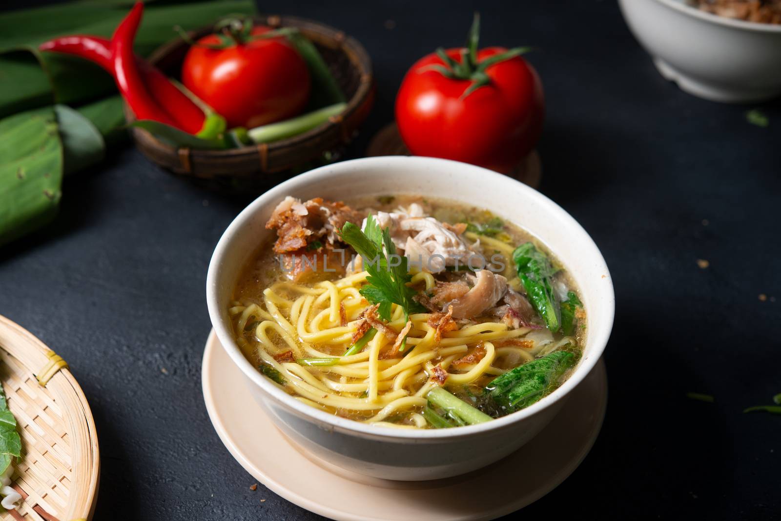 Asian soup noodles and chicken in bowl on dark background. 