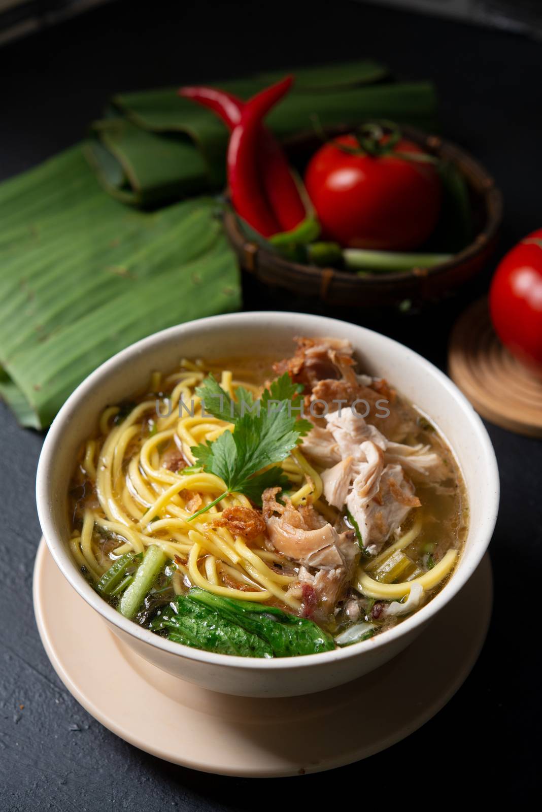 Asian soup noodles and chicken in bowl on dark background. 