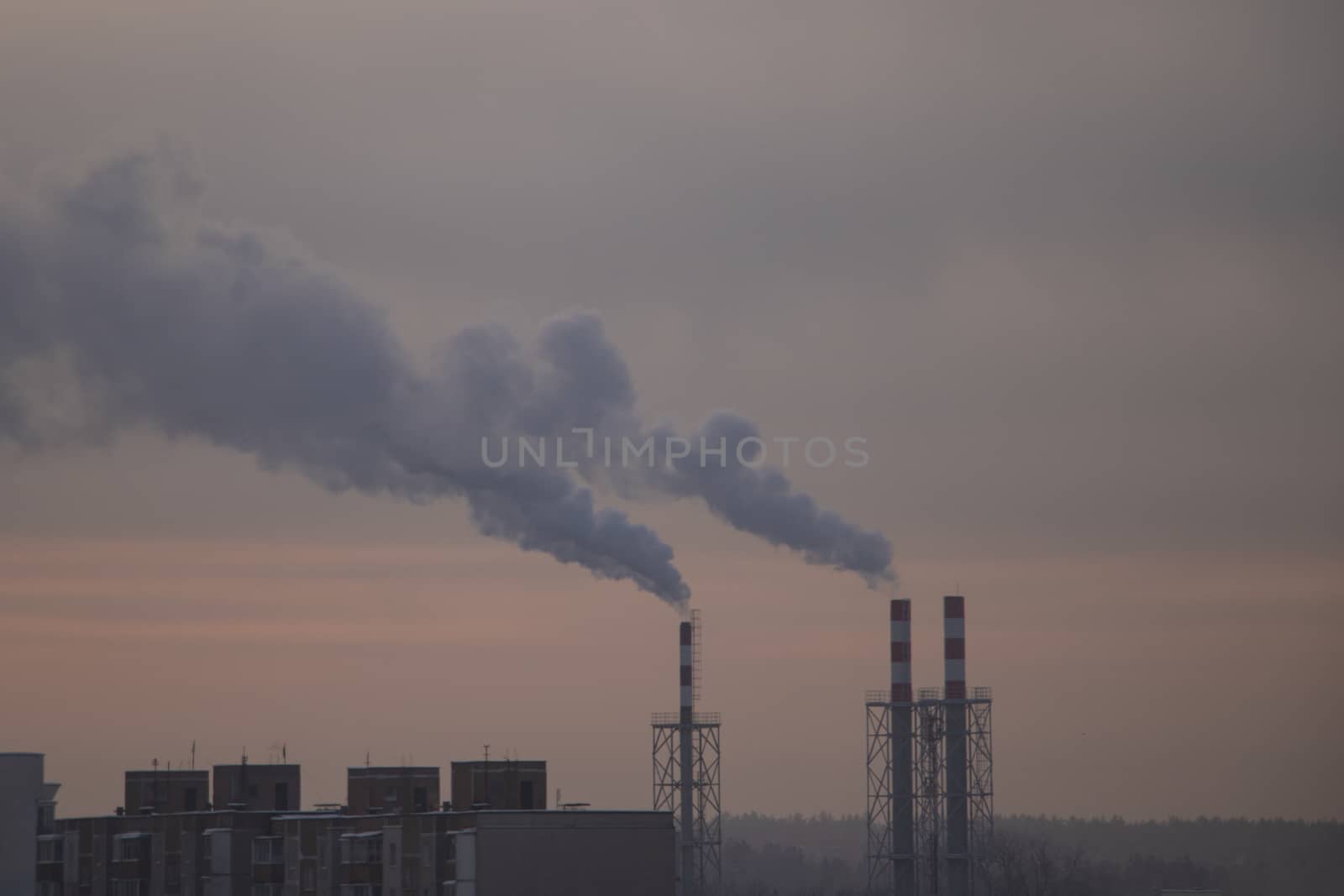 the chimneys of a refinery with smoke and steam with the pink and yellow sunset on the background. by kip02kas