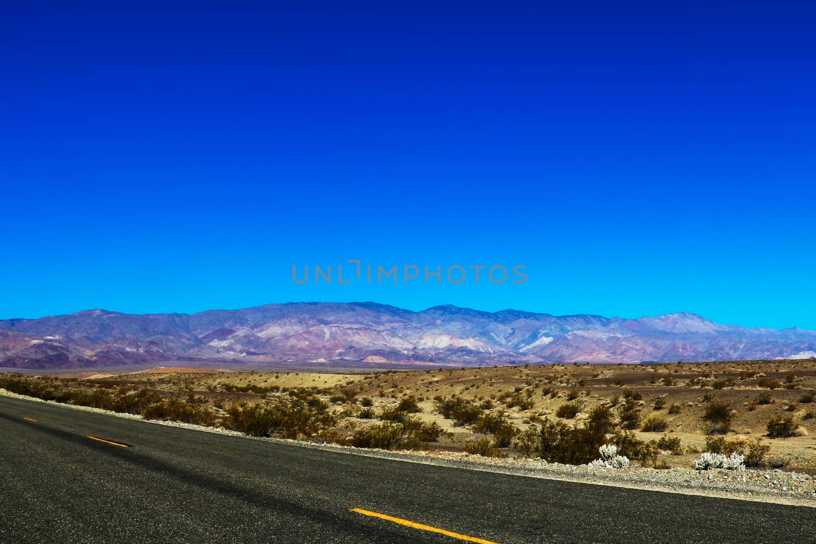 Classic vertical panorama view of an endless straight road running through the barren scenery of the American Southwest with extreme heat haze on a beautiful hot sunny day with blue sky in summer.