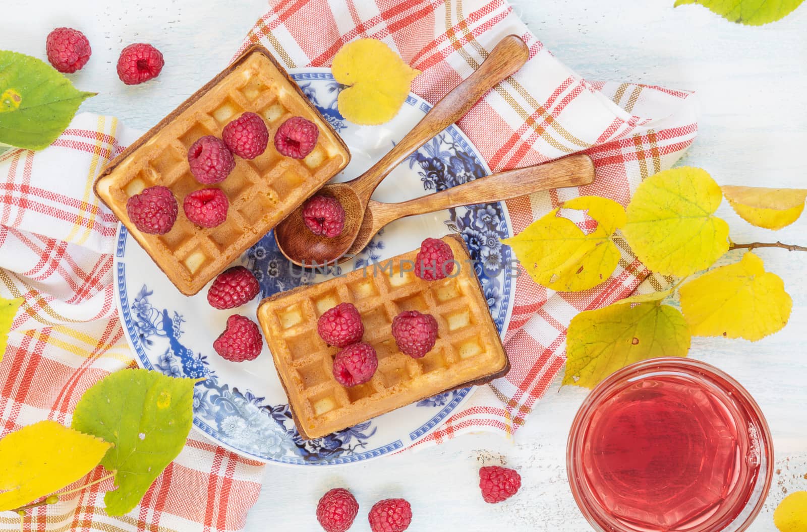 Autumn breakfast with waffles, fresh raspberries and glass of tea, standing on a crumpled checkered napkin