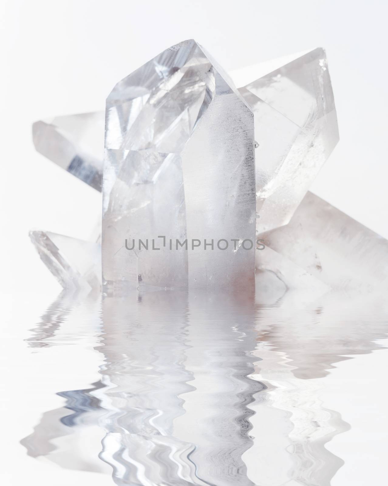 Cluster of several transparent quartz crystals close-up on a white background reflected in a water surface with small waves