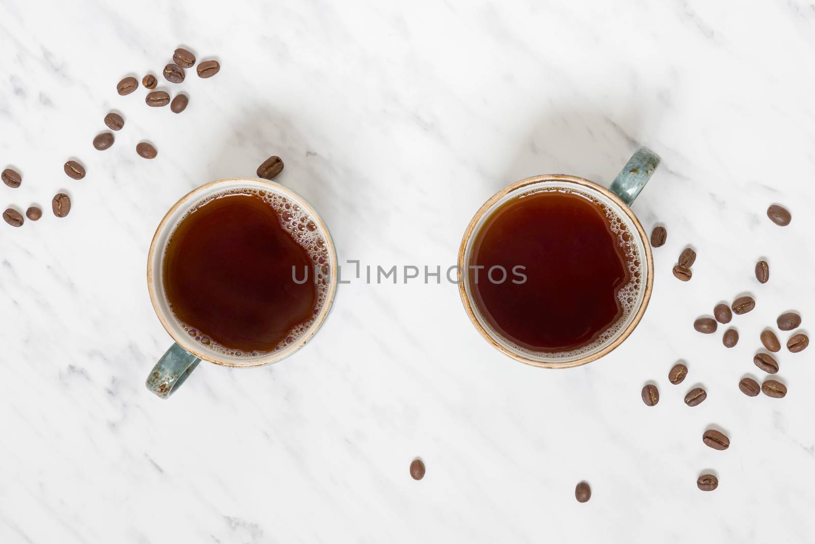 Morning composition with two cups of black coffee and coffee beans on a marble surface with space for text, top view