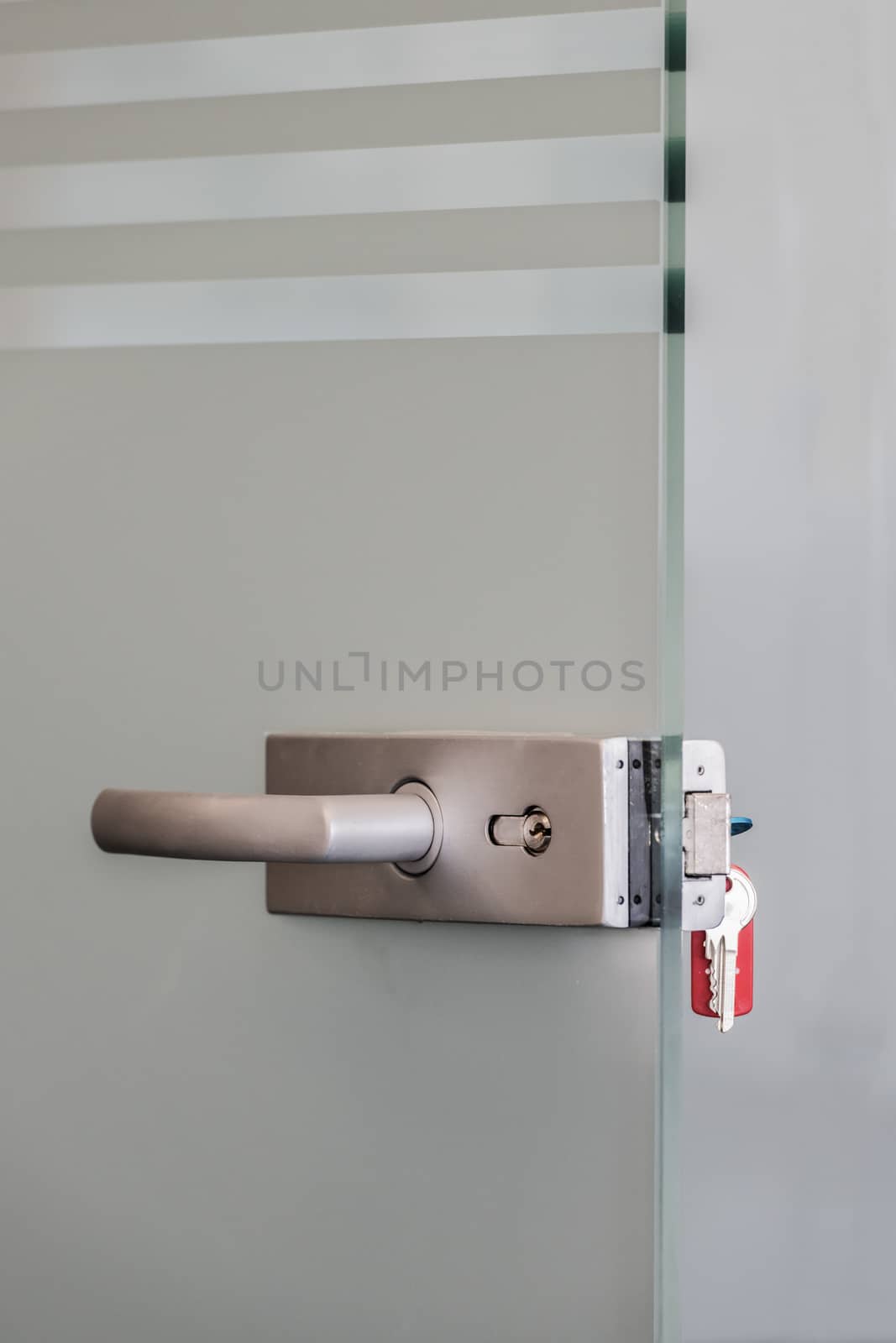 Modern glass door with metal alloy handles and key chain in lock, home or office security concept by asafaric