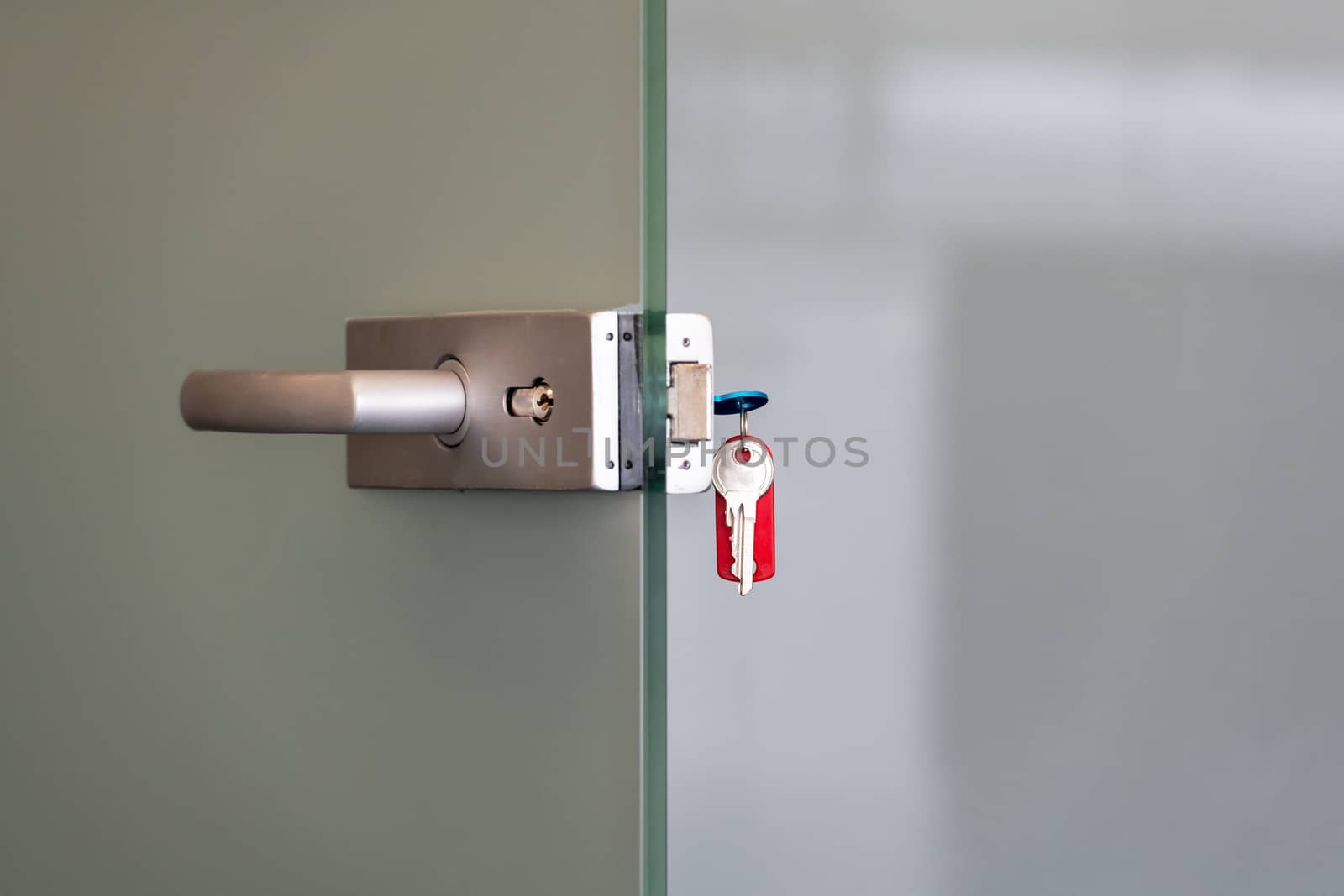 Modern glass door with metal alloy handles and key chain in lock, home or office security concept by asafaric