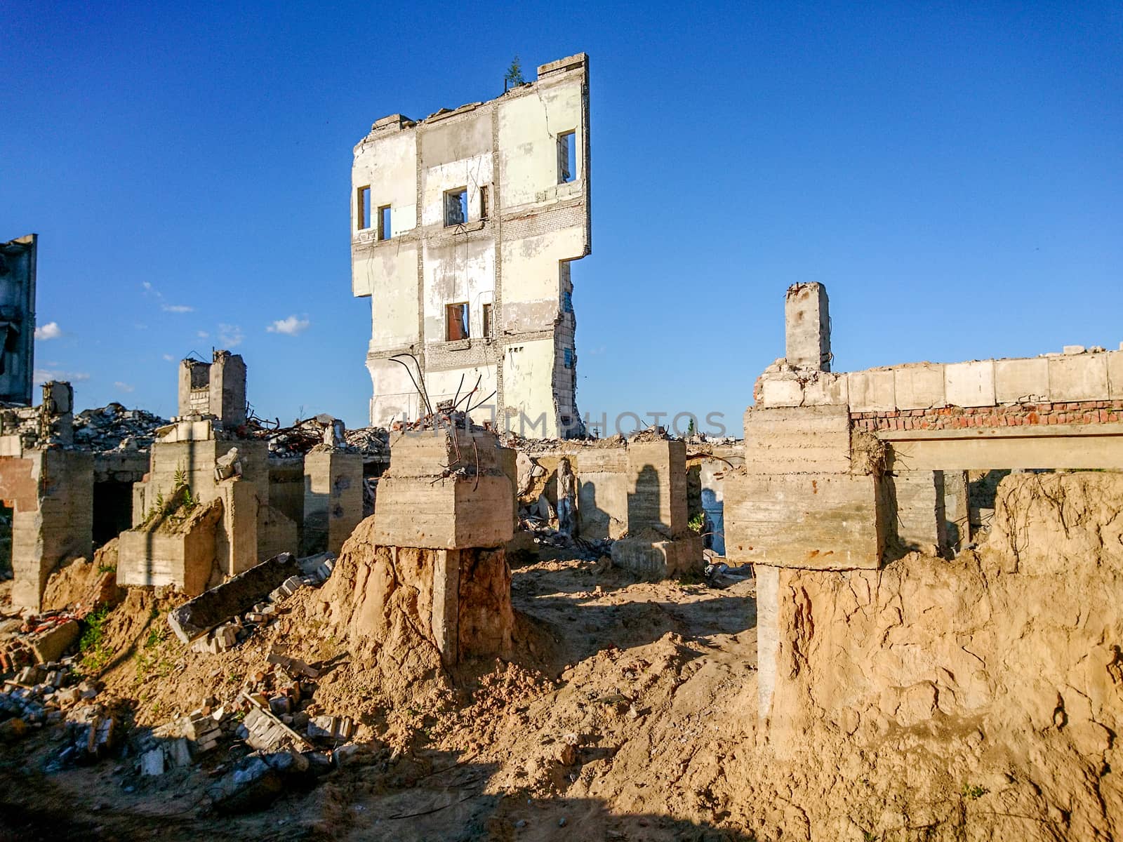 The ruins of a large destroyed building, pieces of stone, concrete, clay and metal against the blue clear sky
