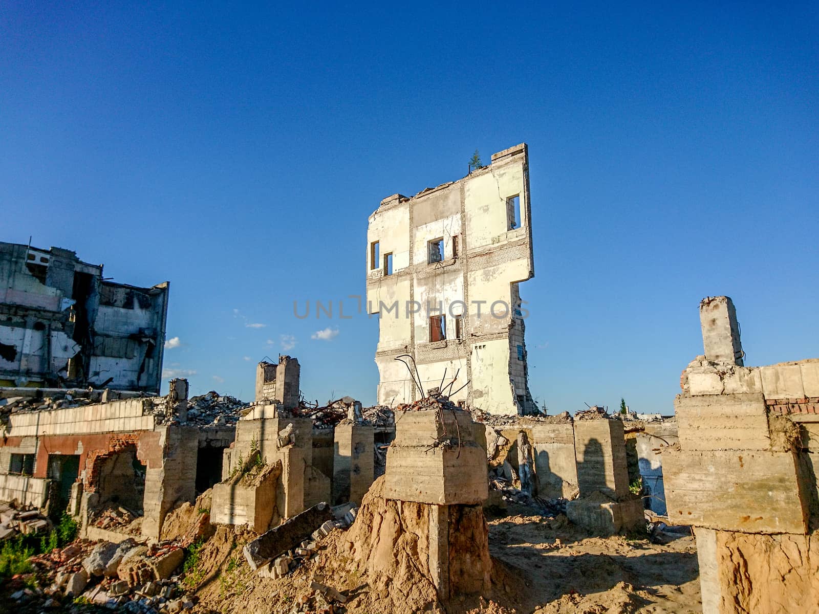 The ruins of a large destroyed building, pieces of stone, concrete, clay and metal against the blue clear sky