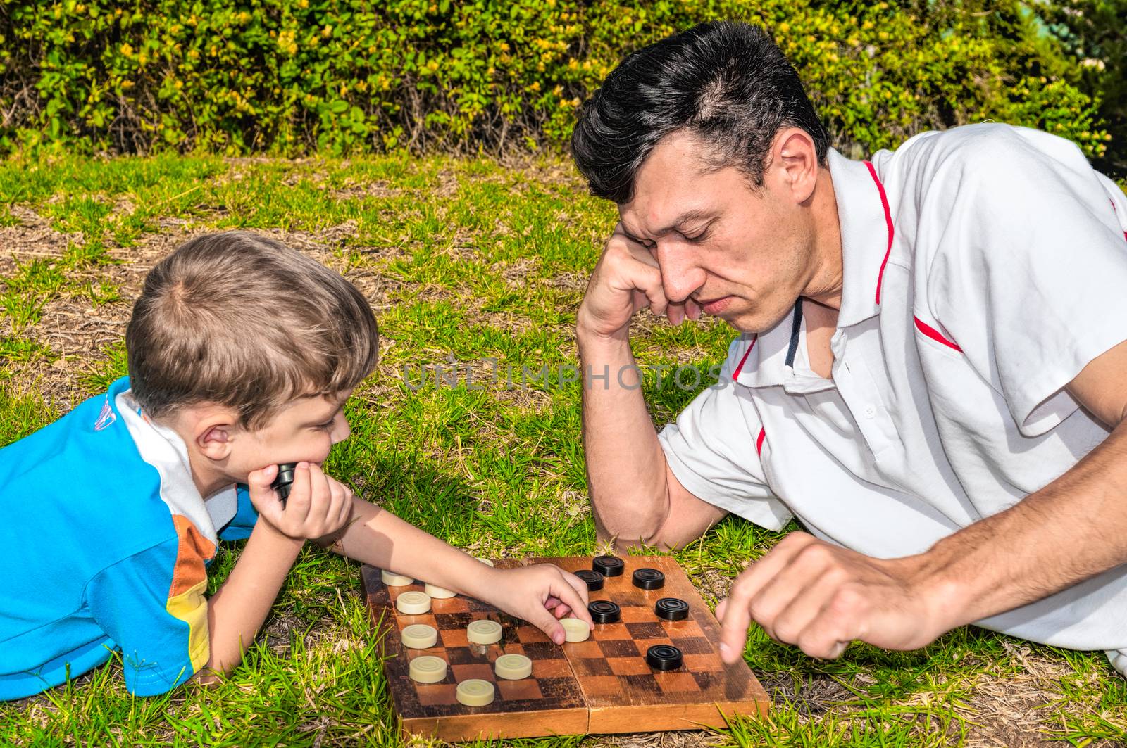 Father and son playing checkers on the grass in a city park