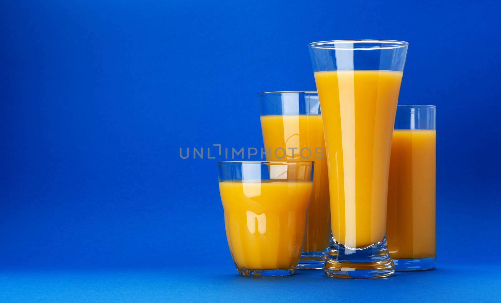 Orange juice in glass isolated on blue background with copy space. Fresh citrus juice, orange cocktail, healthy drink concept, close-up