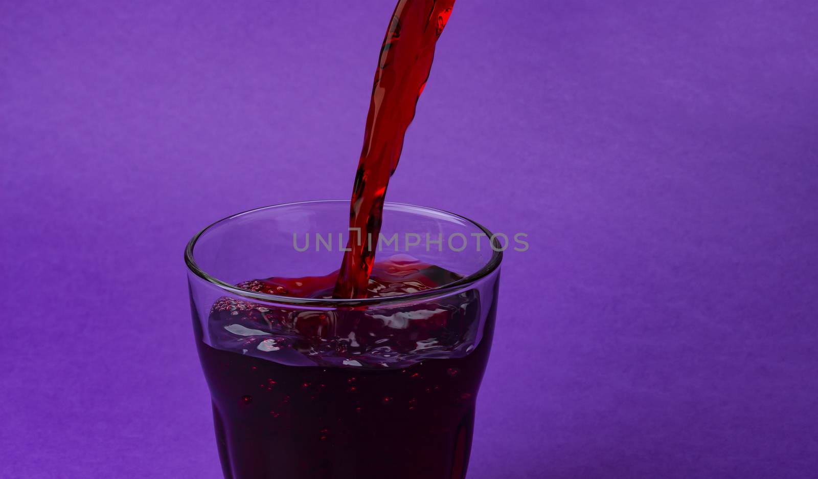 Cherry juice pouring into glass, isolated on purple colour background, with copy space, healthy drink concept, close-up