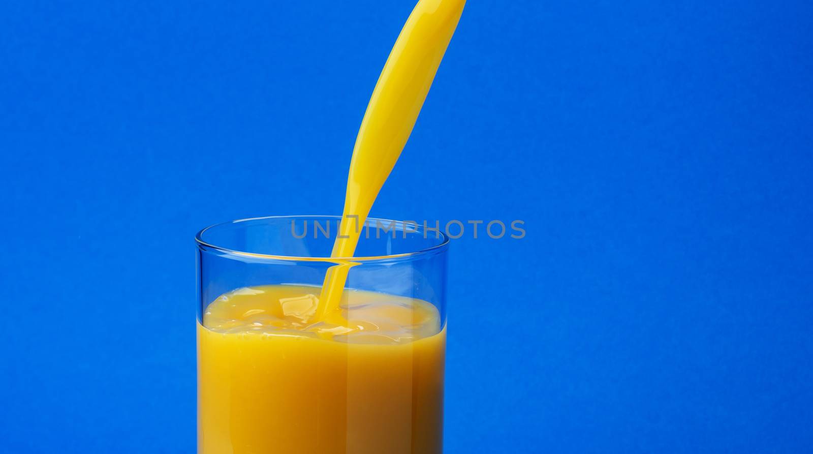 Orange juice pouring into glass, isolated on blue colour background, with copy space, healthy drink concept, close-up