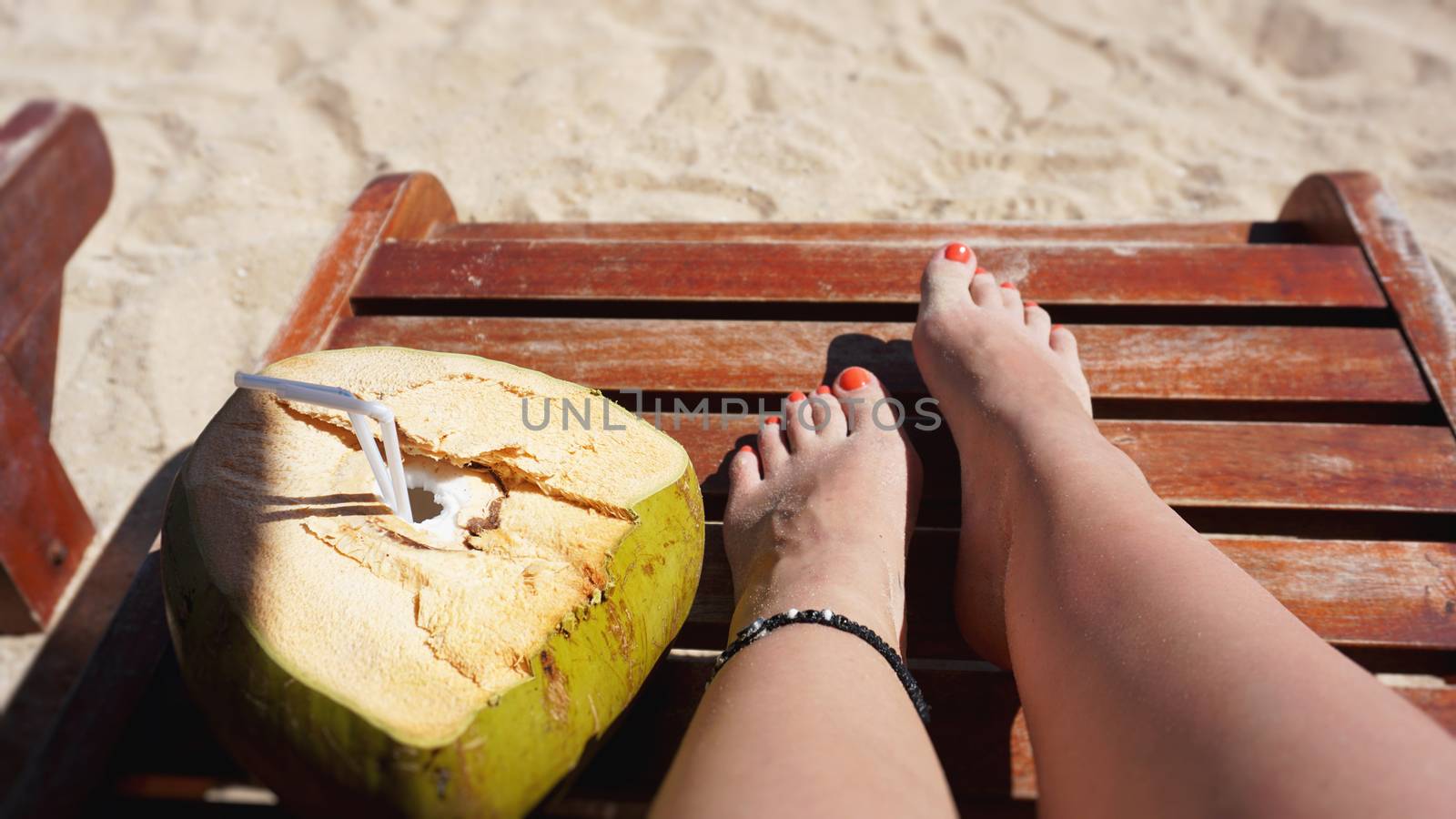 Female legs and coconut drink on the beach, travel and relax
