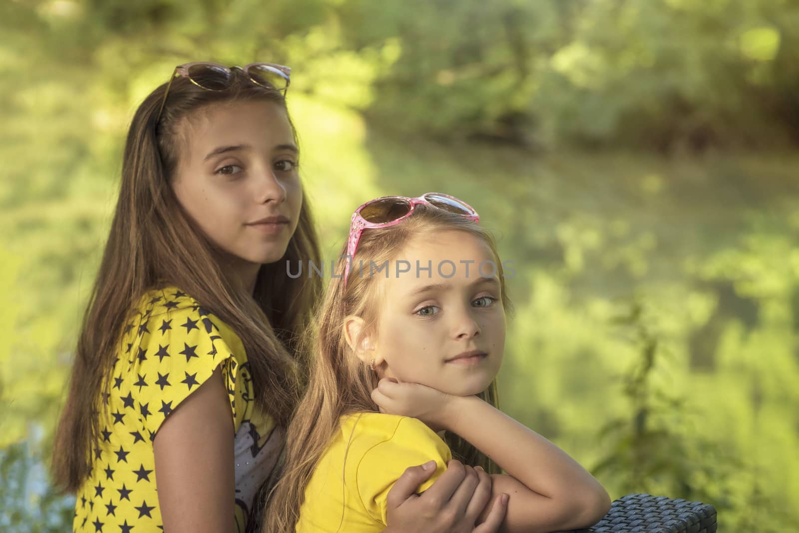 Little sisters in the summer forest Two girls sitting outside on a sunny day.