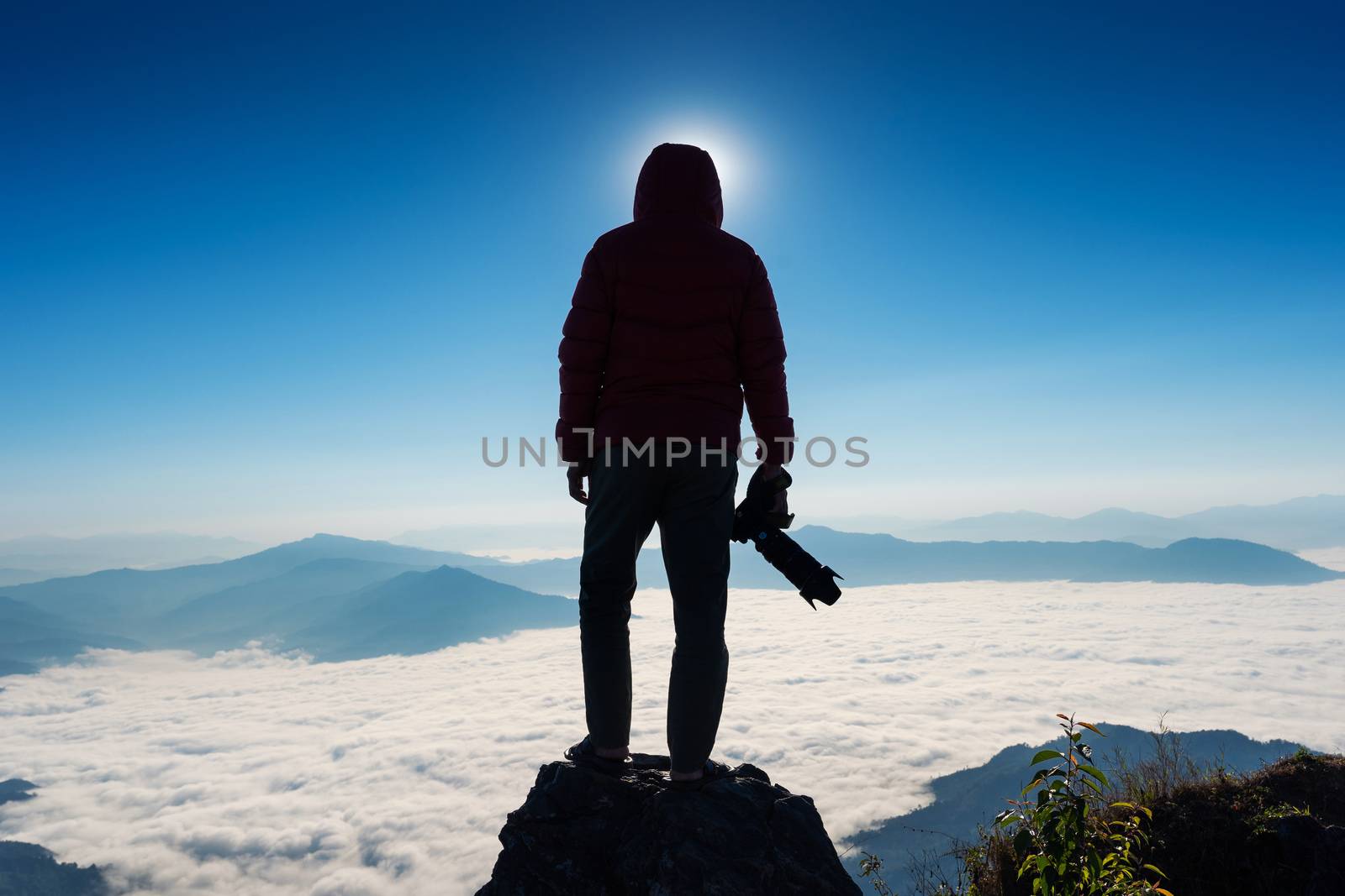 Silhouette of photographer hand holding camera and standing on top of the rock in nature. Travel concept.