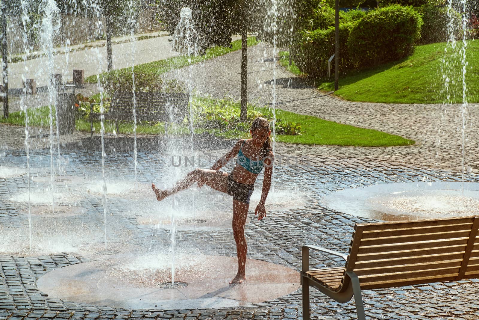 Girl on a sunny summer day are poured water from a fountain.Girl happily in shallow clean water on of city fountain on warm bright summer day.