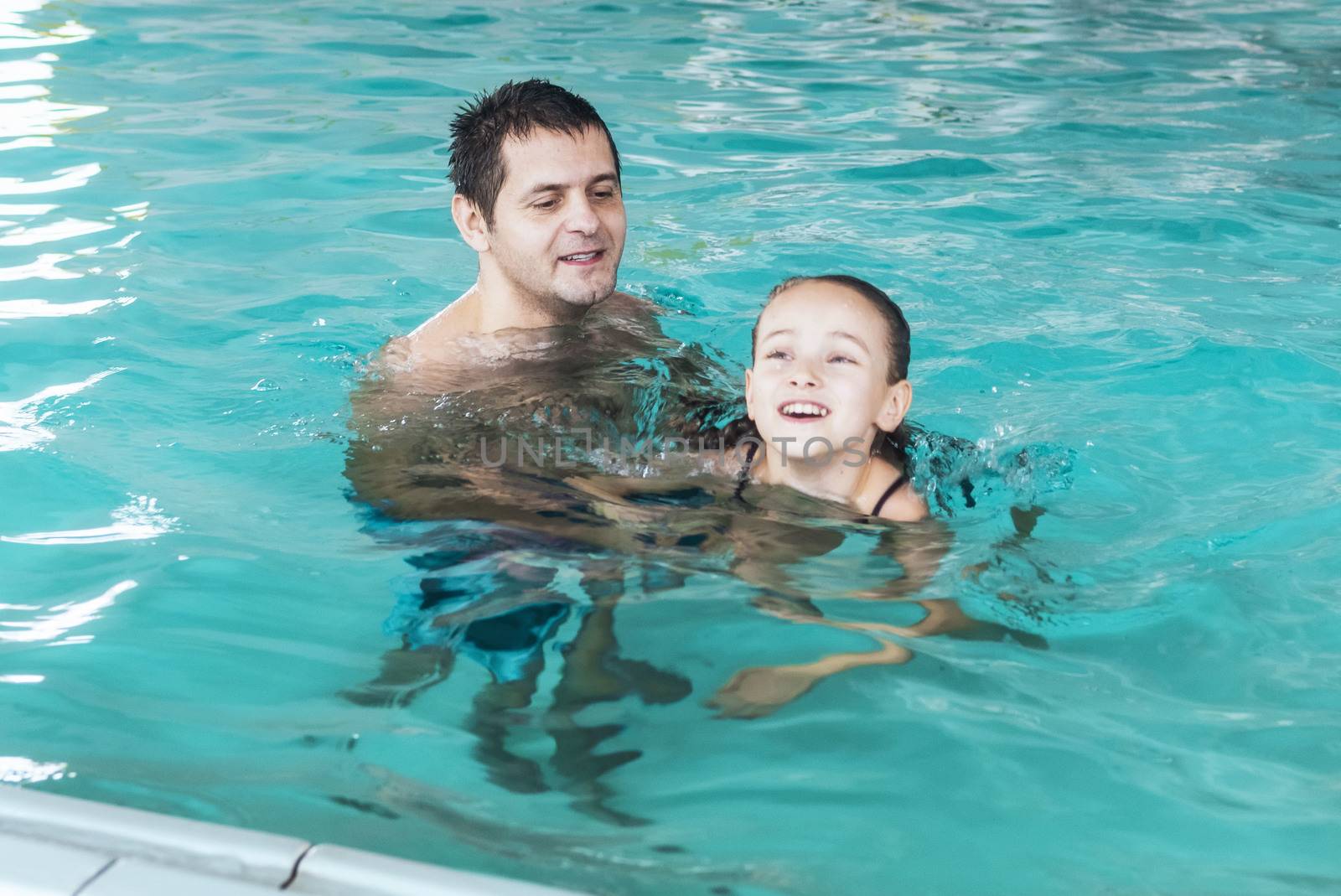 Father teaches girl to swim in the pool. Happy father teaching his little daughter to swim. Active happy child learning to swim. Little girl in a pool .