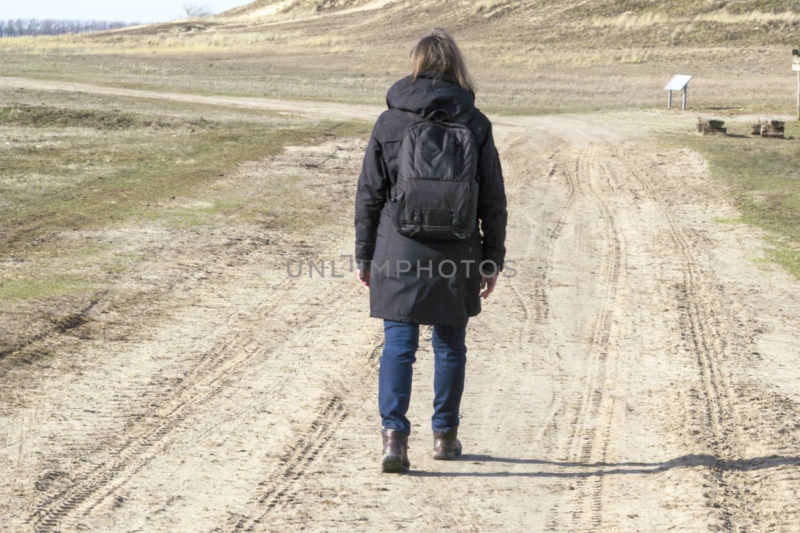 Caucasian woman in black coat arms raised on empty road towards sunset