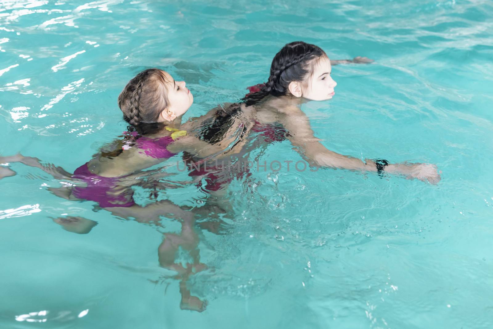 Two sisters in the pool. Two happy girls play in the pool.Beautiful girls swim and having fun in water.Active holiday.Two girls swim in the pool.