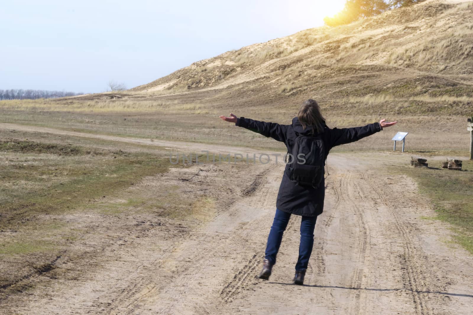 Caucasian woman in black coat arms raised on empty road towards sunset by Fr@nk