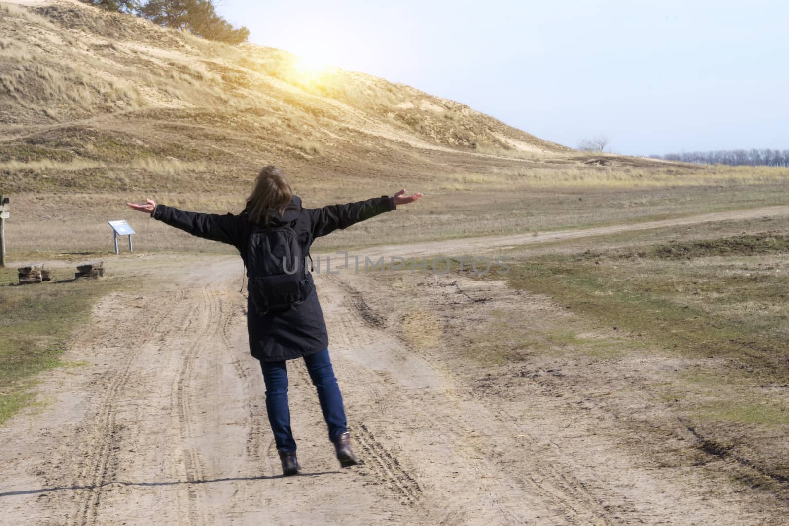 Caucasian woman in black coat arms raised on empty road towards sunset