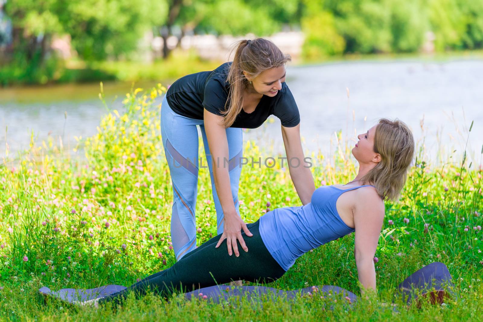 trainer helps to correctly perform yoga exercises to a mature woman, sports in the park in summer