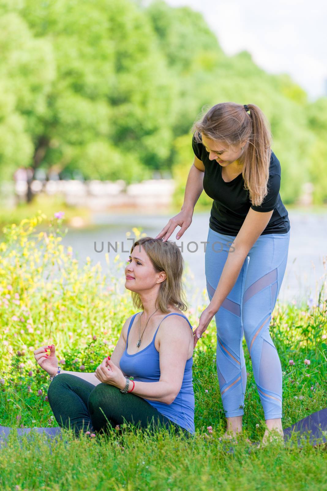 an experienced trainer in yoga helps to sit correctly in the lotus position, sport in summer park