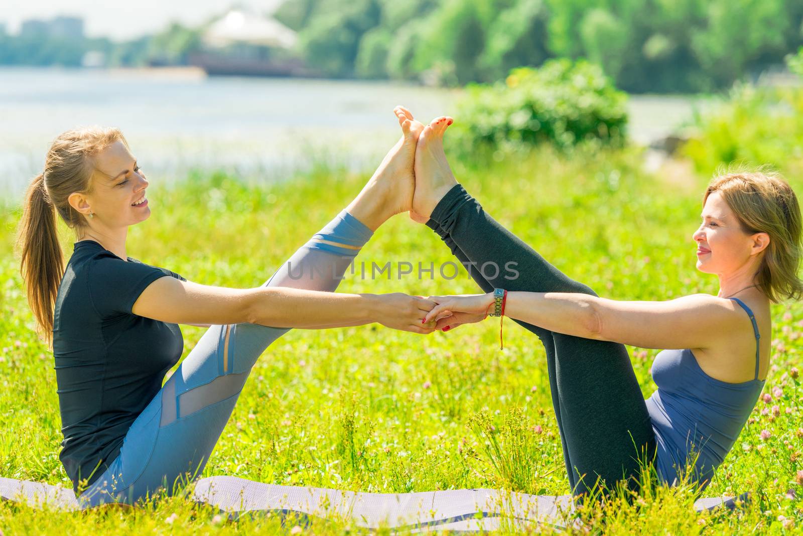 mature woman doing yoga stretching exercises with an individual trainer in the park