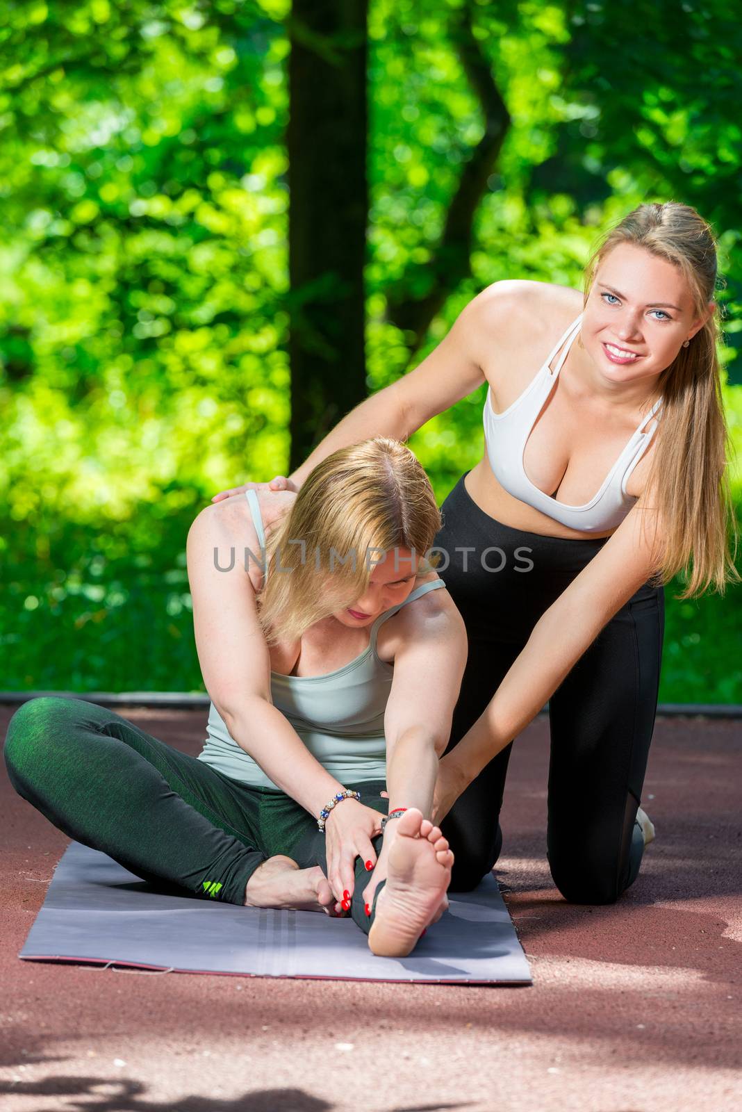 in the park, a yoga trainer helps a woman to do stretching exercises