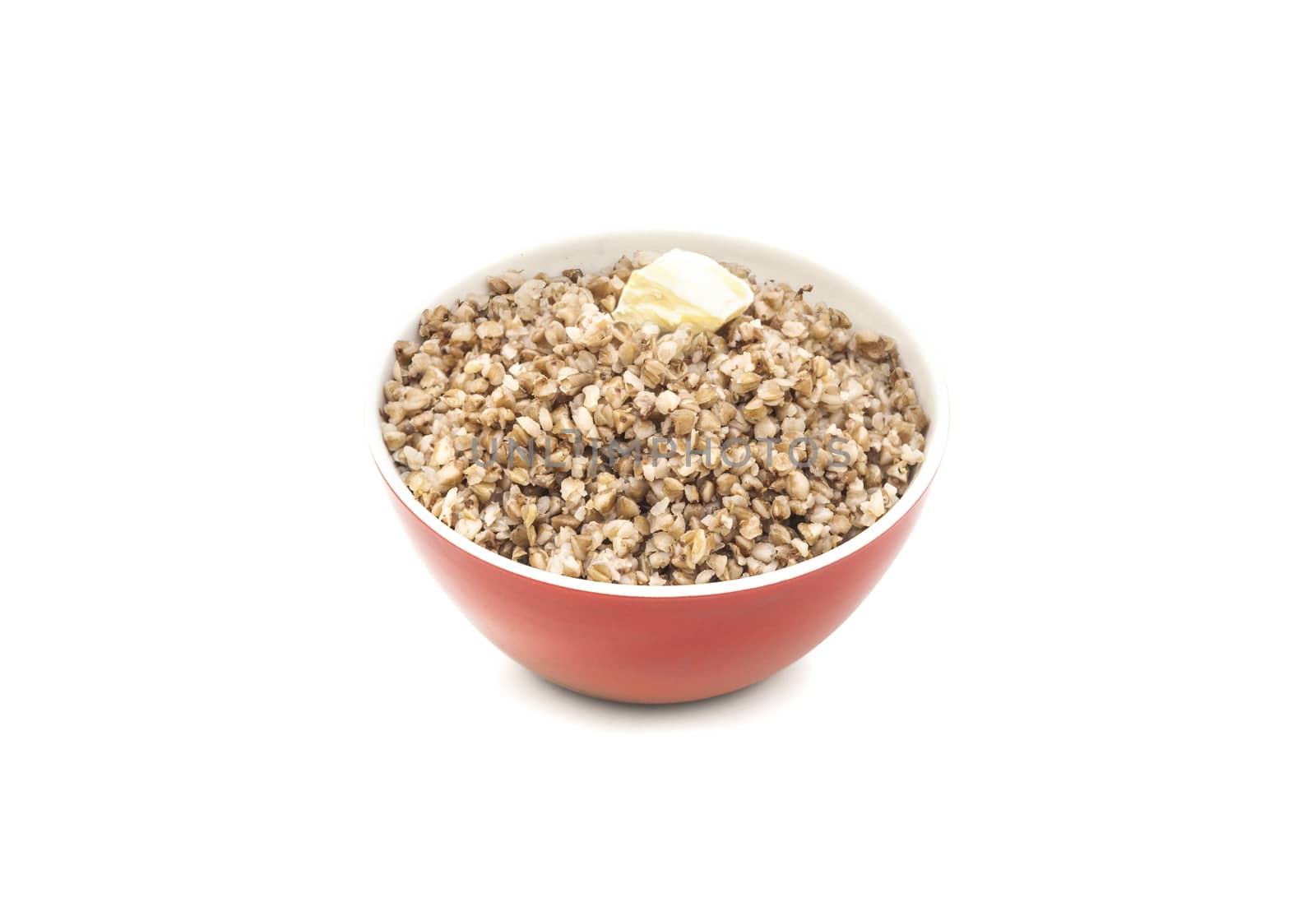 Dry buckwheat in red ceramic bowl with a piece of butter. Isolated on white background.