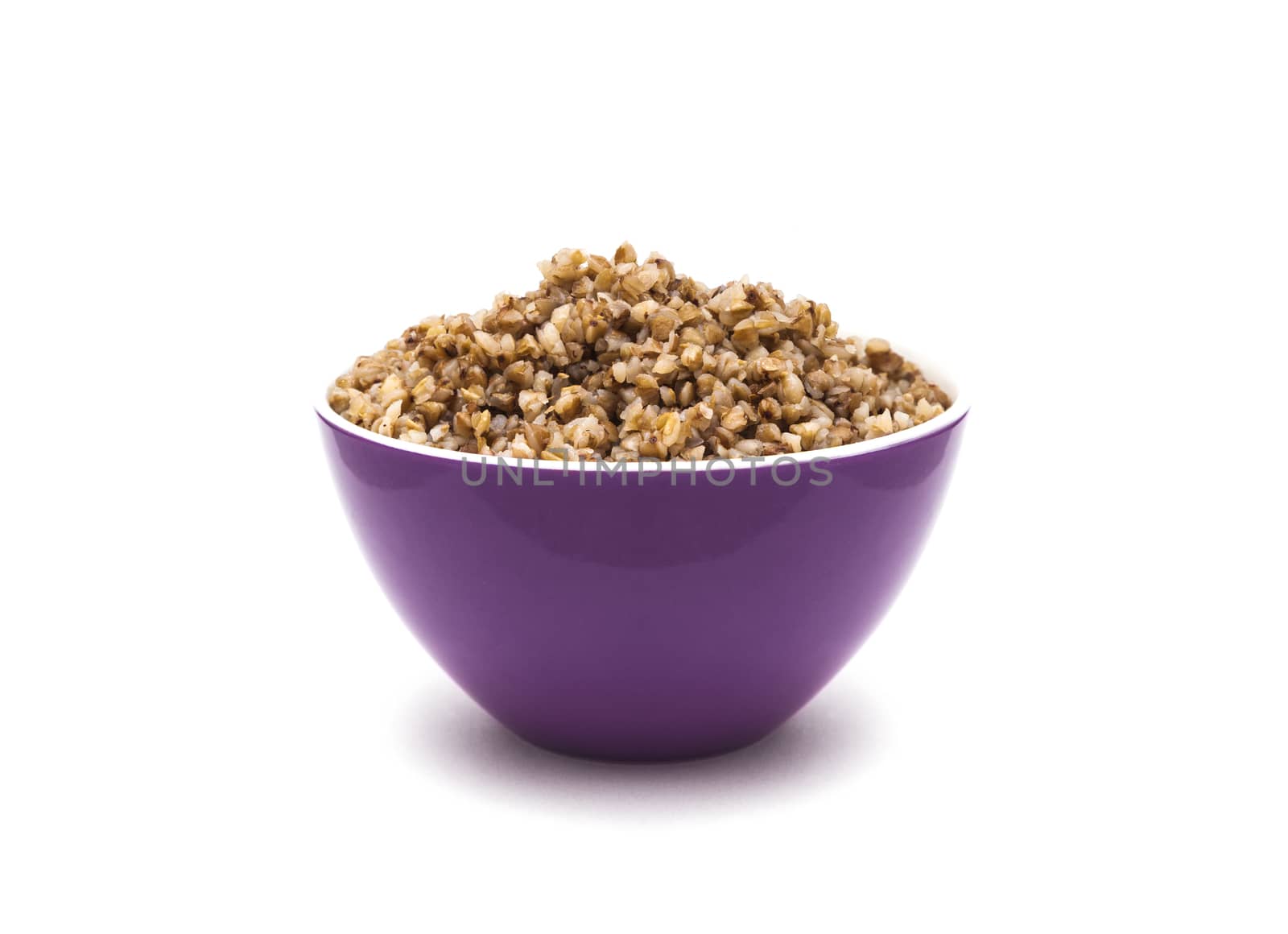 Dry buckwheat in purple ceramic bowl isolated on white background. Isolated on white background.