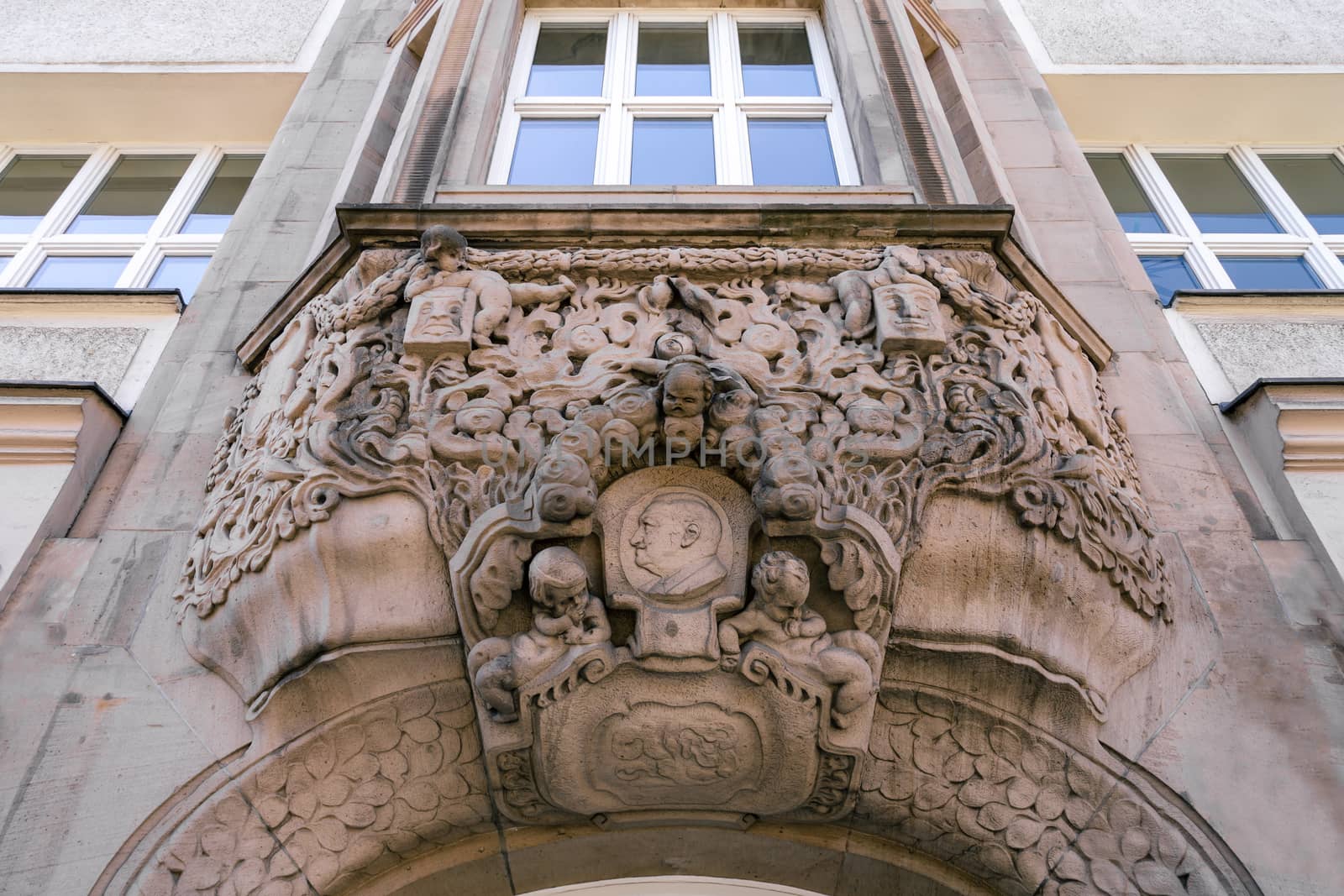 Detailed sculptural decoration of the gable and arched entrance in the Baroque style. Figures carved in stones adorn the entrance of a building with historical details in the city of Berlin.