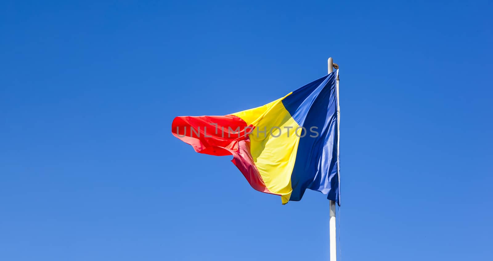 Romanian Flag on the mast. Romania flag of silk. Romanian flag on flagpole blowing in wind isolated against blue sky with copyspace.