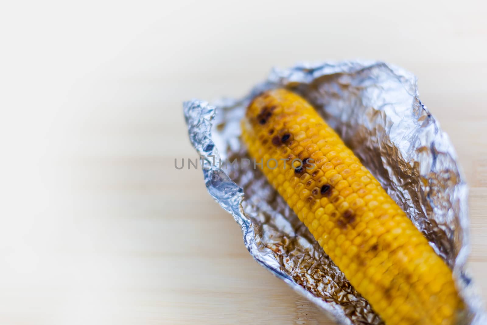 Baked yellow corn in foil on white wooden background