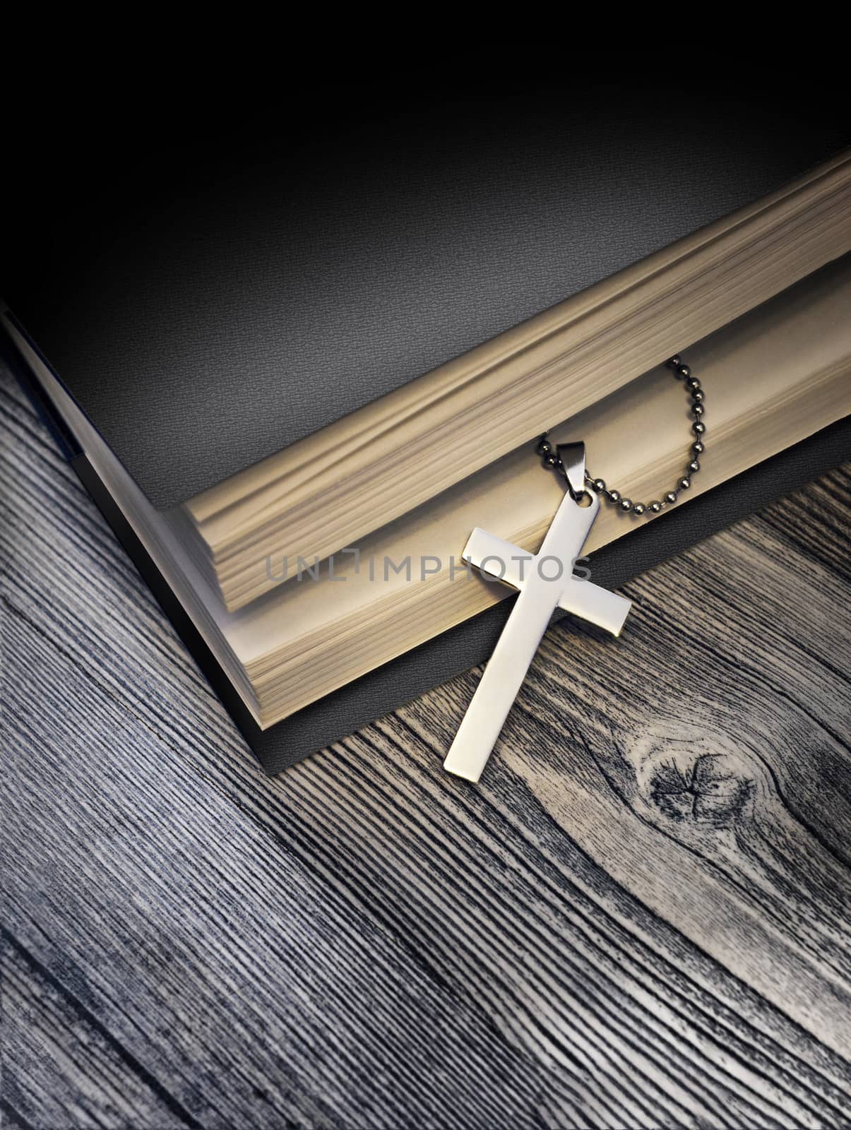 Metal cross on top of a black book cover on wooden background